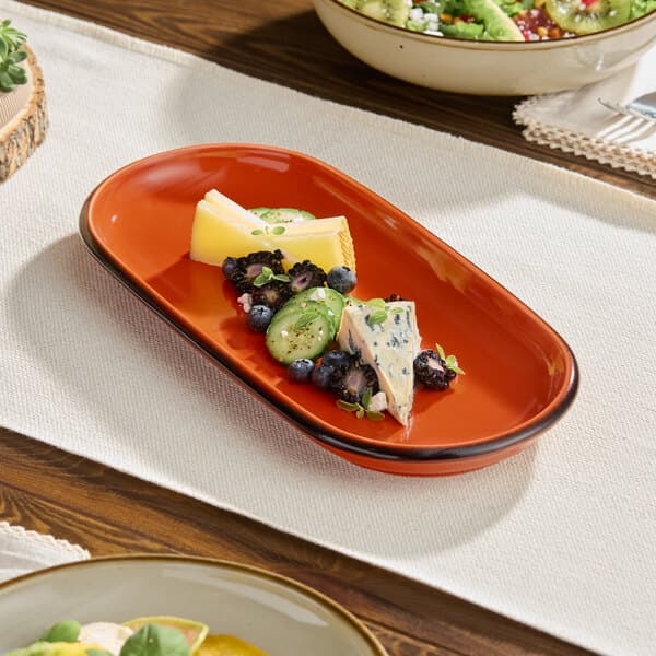 An orange stoneware oblong coupe platter with a sample serving of cheese, fruit, and herbs.