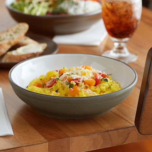 An Acopa Embers moss green stoneware pasta bowl filled with pasta, cheese, and tomatoes on a table.