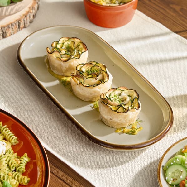 An oblong granite gray stoneware platter with a coupe edge, displayed with three pastry appetizers.