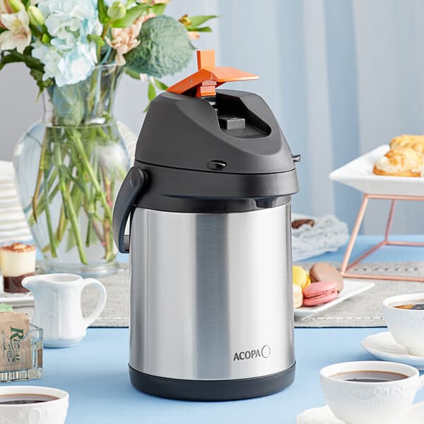 An Acopa stainless steel decaf airpot on a table with a cup of coffee.