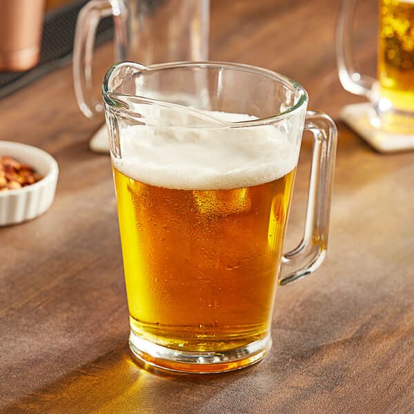 An Acopa glass pitcher of beer on a table.