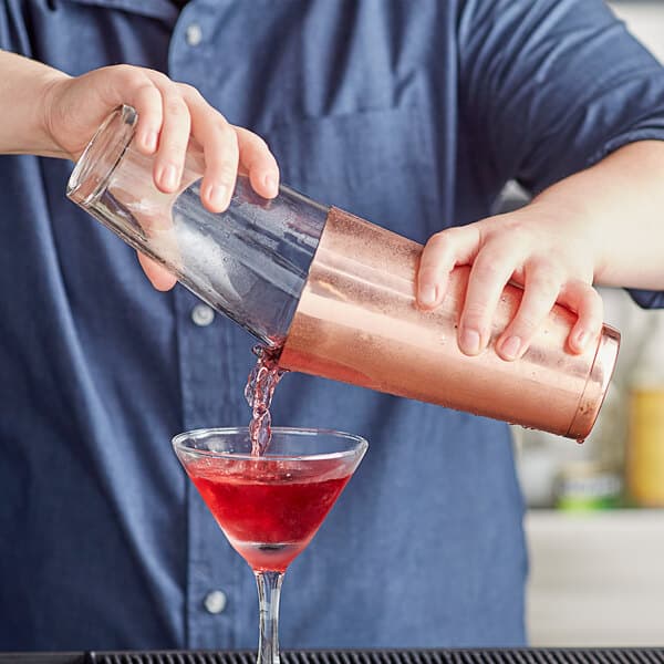 A bartender using an Acopa copper cocktail shaker to pour a drink.