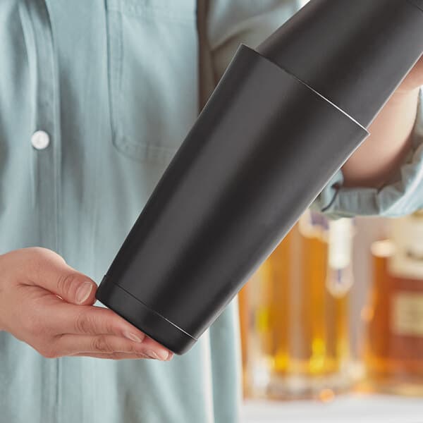 A person holding a black cocktail shaker tin.
