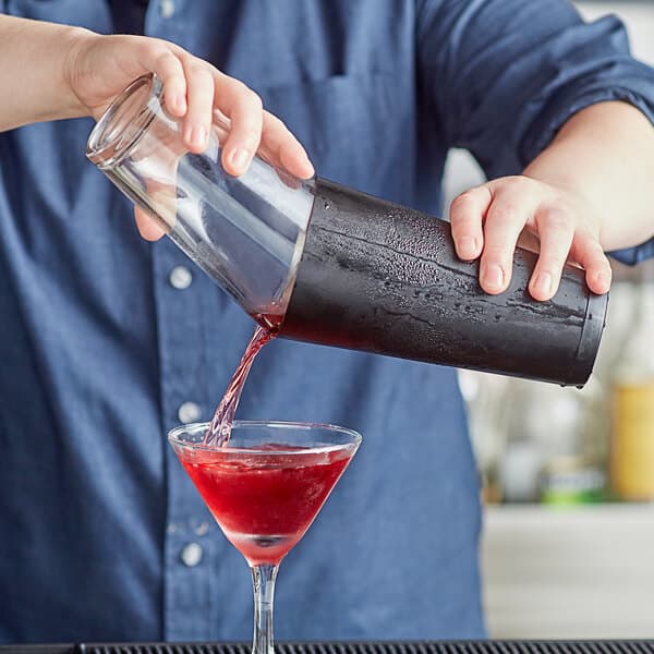 A man using an Acopa full size cocktail shaker tin to pour a drink into a glass.