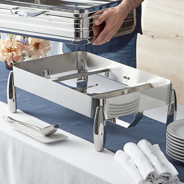 A person holding a metal container on a silver tray with a plate on it.