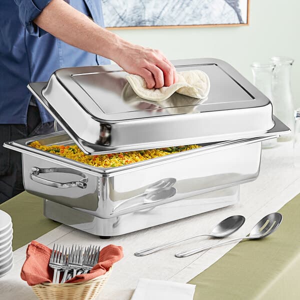 A man preparing a large Acopa stainless steel electric chafing dish on a table.