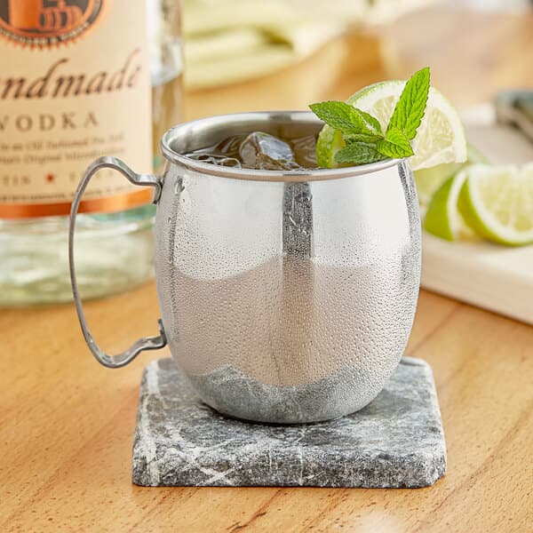 An Acopa silver Moscow Mule mug filled with ice and mint leaves on a marble coaster.