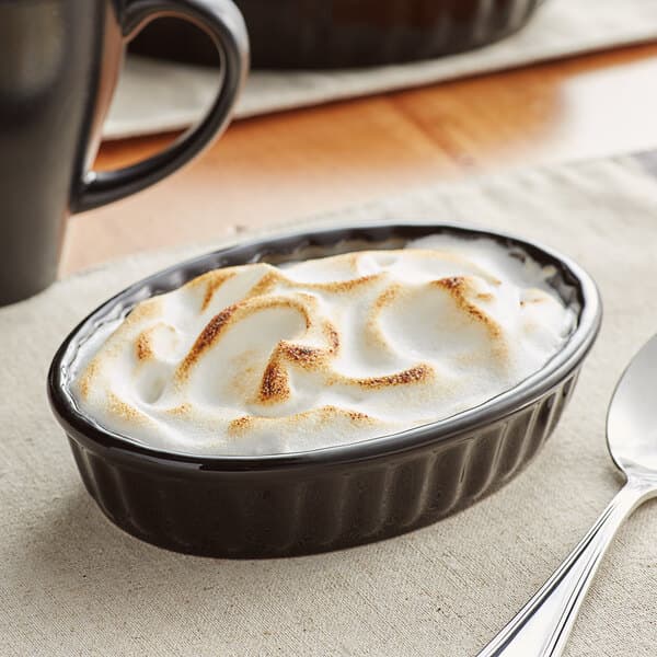 An Acopa glossy black fluted oval dish with food in it.