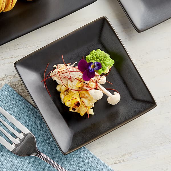 A Acopa matte black square stoneware plate with food and a fork on a table.
