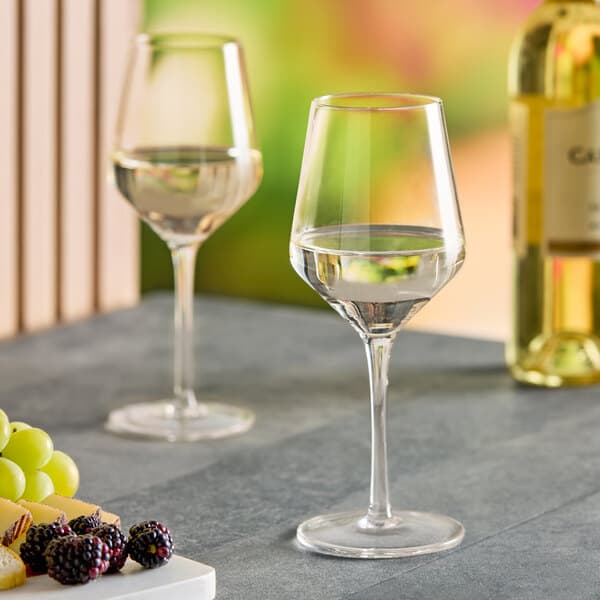 Two Acopa Silhouette wine glasses on a table next to a bottle of wine.