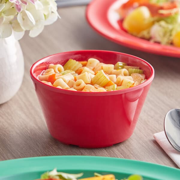 An Acopa red melamine bouillon cup filled with soup and vegetables on a white surface.