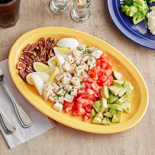 A yellow Acopa Foundations narrow rim oval platter with food on it.