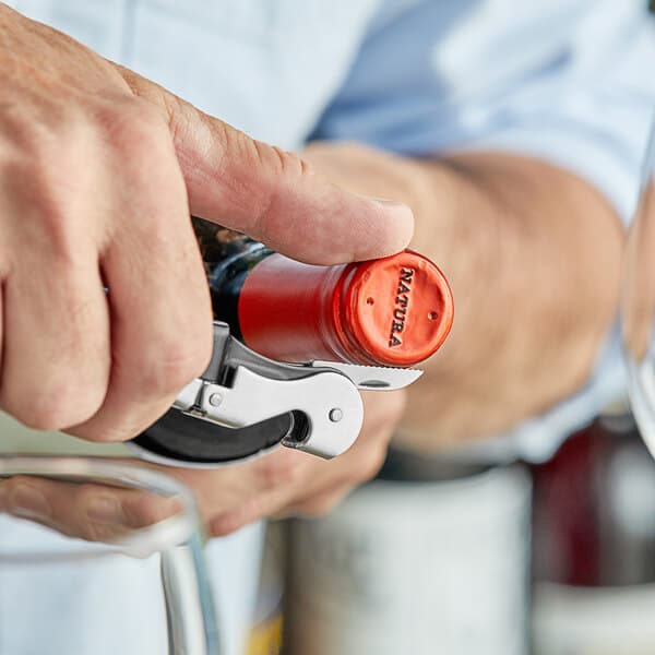A person using an Acopa waiter's corkscrew with a black metal handle to open a bottle of wine.