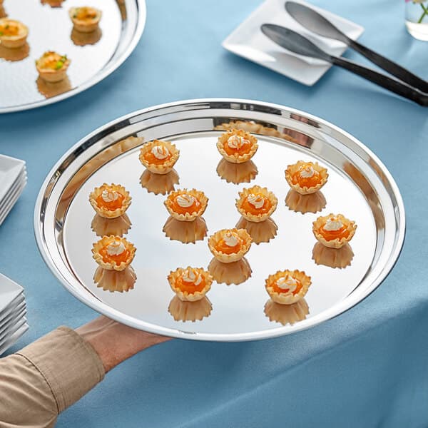 A person's hand holding an Acopa stainless steel catering tray of food.