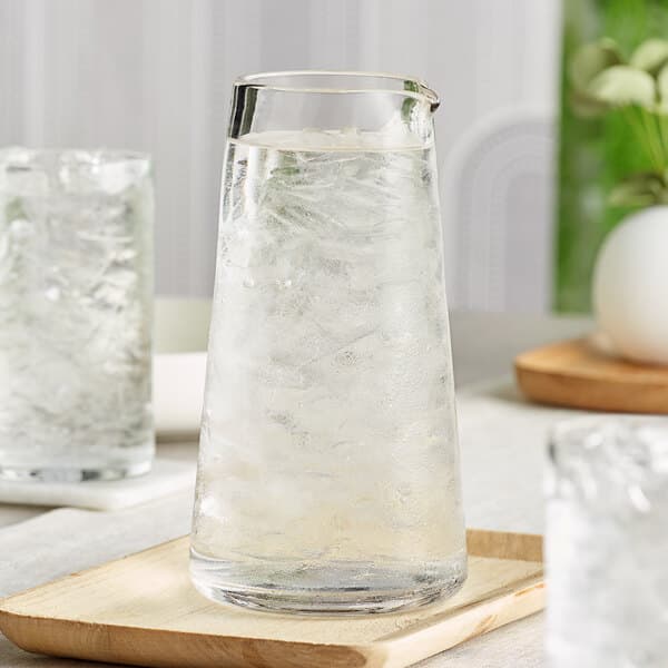 An Acopa Pangea glass carafe of water with a glass of ice on a wooden tray.