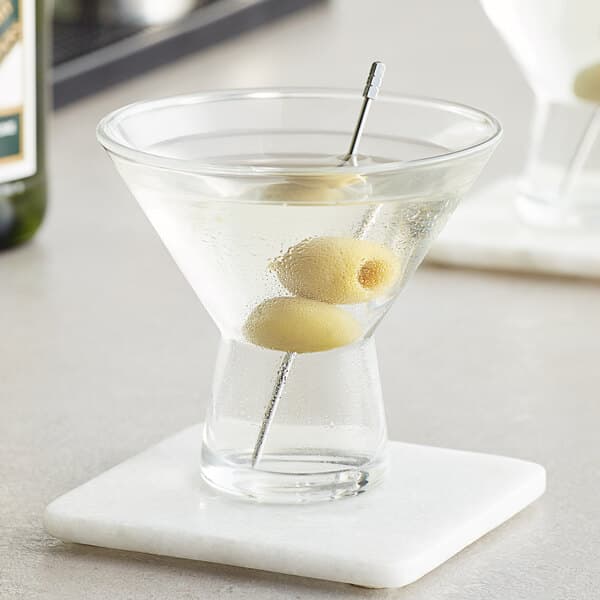 Two Acopa martini glasses filled with liquid and olives on a counter.