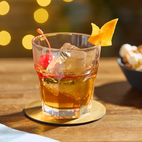 An Acopa Memphis old fashioned glass filled with brown liquid, ice, and a cherry.
