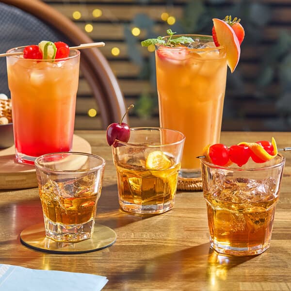 Acopa Memphis beverage glasses filled with orange drinks, ice, and oranges on a table.