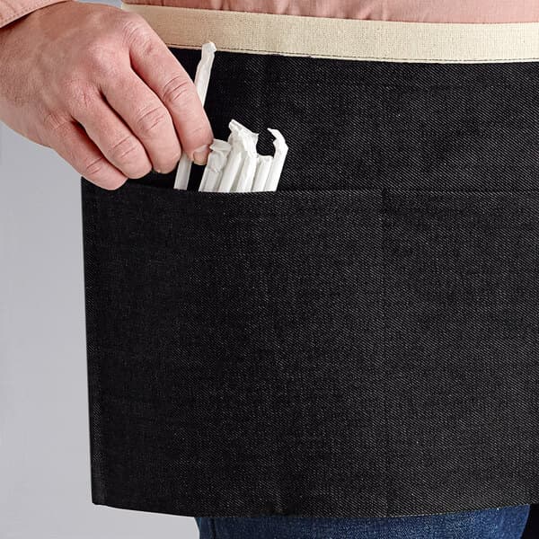 A person using an Acopa Kennett black denim waist apron with natural webbing to hold straws.