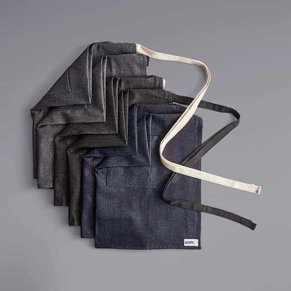 Acopa Kennett grey and black denim aprons stacked on a table.