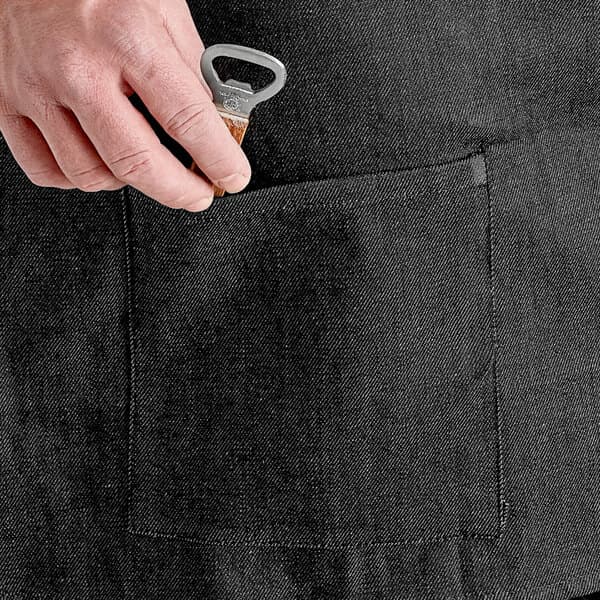 A person using an Acopa Kennett black denim half bistro apron with black webbing and pockets to open a bottle of wine.