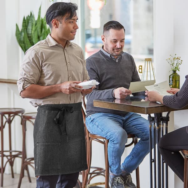 A man wearing an Acopa black denim half bistro apron sitting at a table.