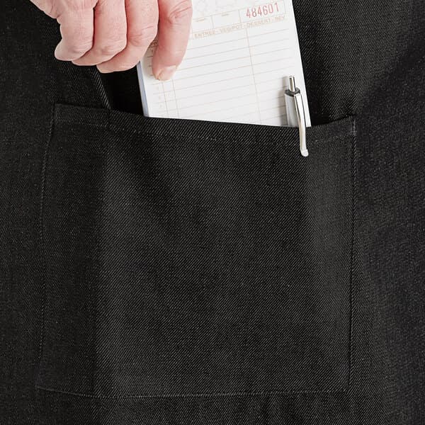 A person's hand putting a receipt in the pocket of a black Acopa bistro apron.