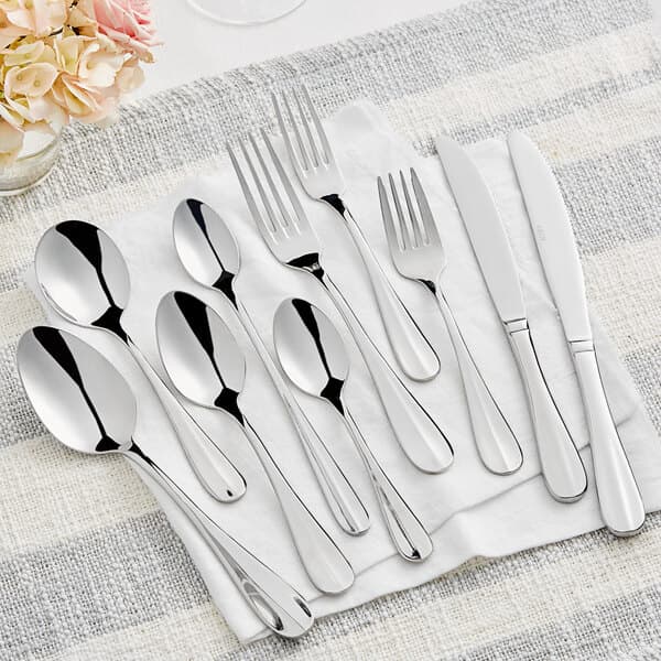 An Acopa stainless steel spoon next to a fork and knife on a napkin.