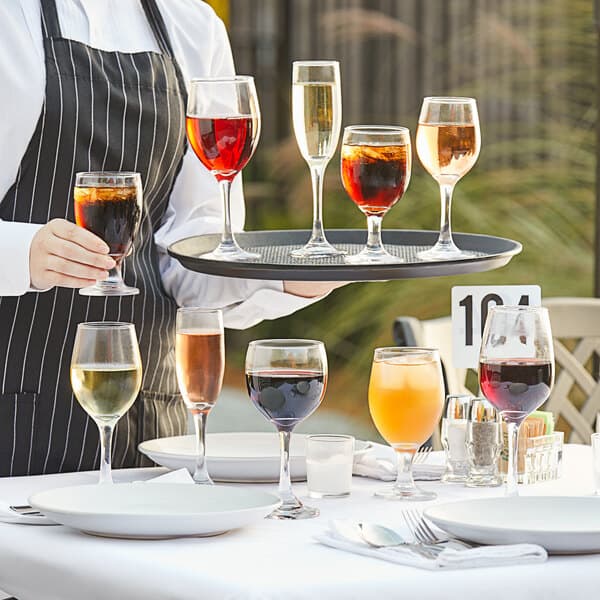 A waiter holding a tray with Acopa 8 oz. wine glasses filled with red wine.