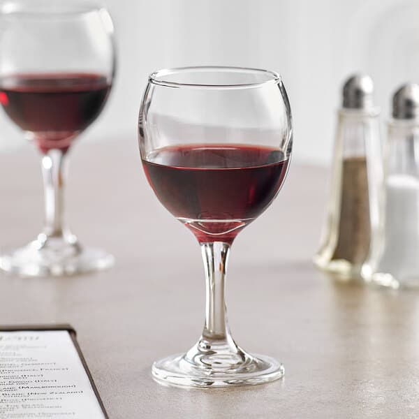 Two Acopa all-purpose wine glasses on a table with a glass of red wine.