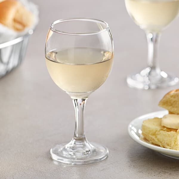 An Acopa 8 oz. wine glass filled with white wine next to a plate of food.