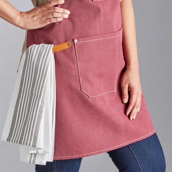 A woman wearing an Acopa Hazleton wine canvas bib apron holding two towels.