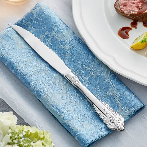 An Acopa Ophelia steak knife on a blue napkin next to a plate of food.