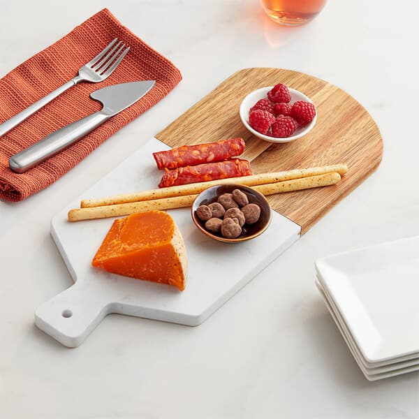 An Acopa acacia wood and marble serving board with cheese, nuts, and snacks on it.