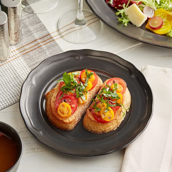 An Acopa Condesa armor gray porcelain plate with bread, tomatoes, and salad on a table.