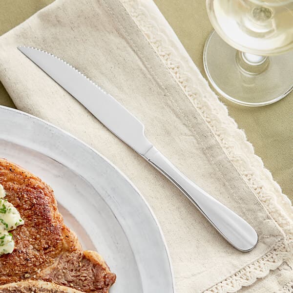A plate with a steak and an Acopa Brigitte stainless steel steak knife on it.
