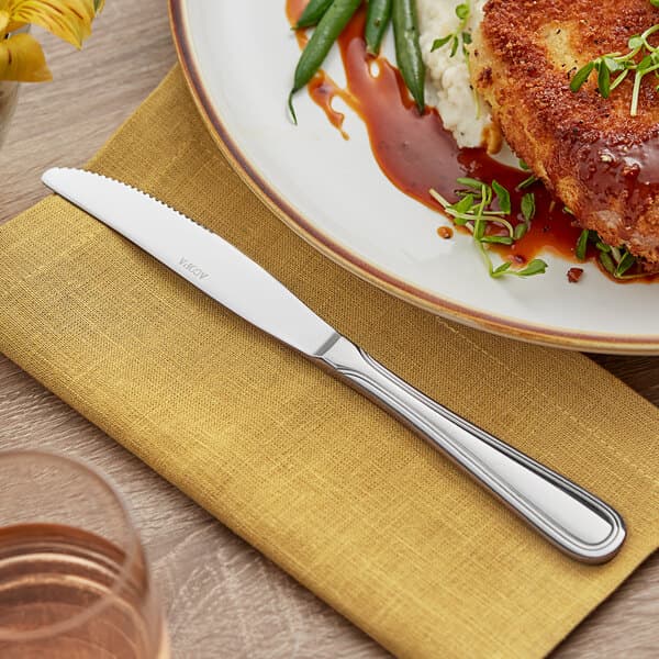 An Acopa Edgewood stainless steel dinner knife on a plate of food with green beans and sauce.