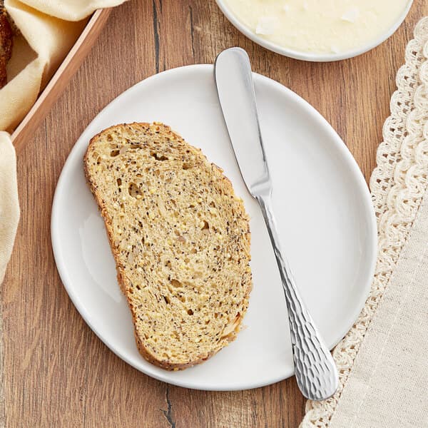 A slice of bread on a white plate with an Acopa Inspira stainless steel butter knife.