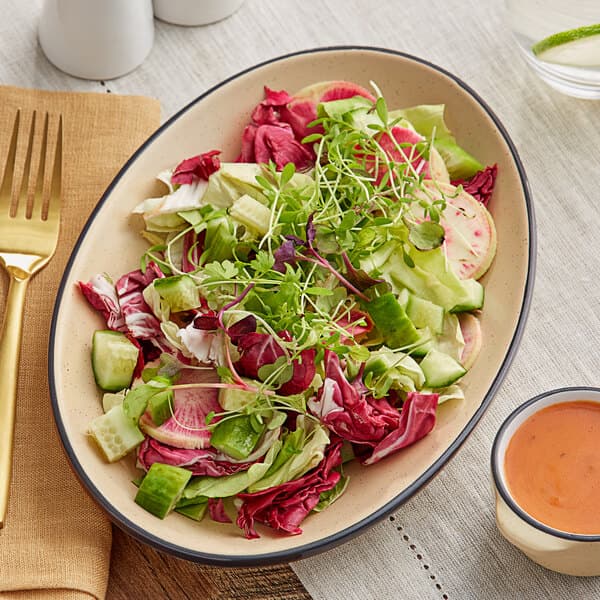 An Acopa Harvest Tan matte coupe stoneware platter with salad on a table.