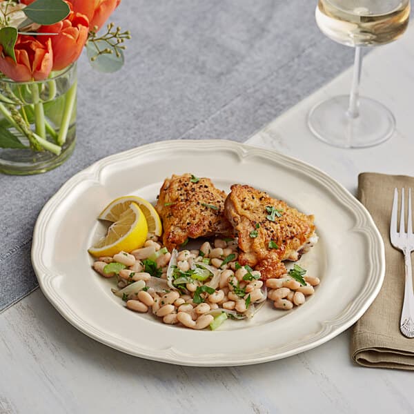 A plate of food with a glass of wine and a vase of flowers on an Acopa Condesa porcelain plate.