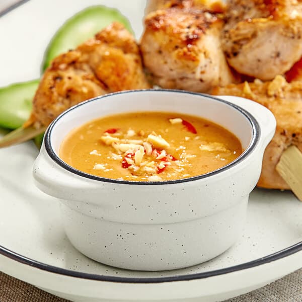 A hand dipping chicken skewers into sauce in a grey matte stoneware sauce cup.