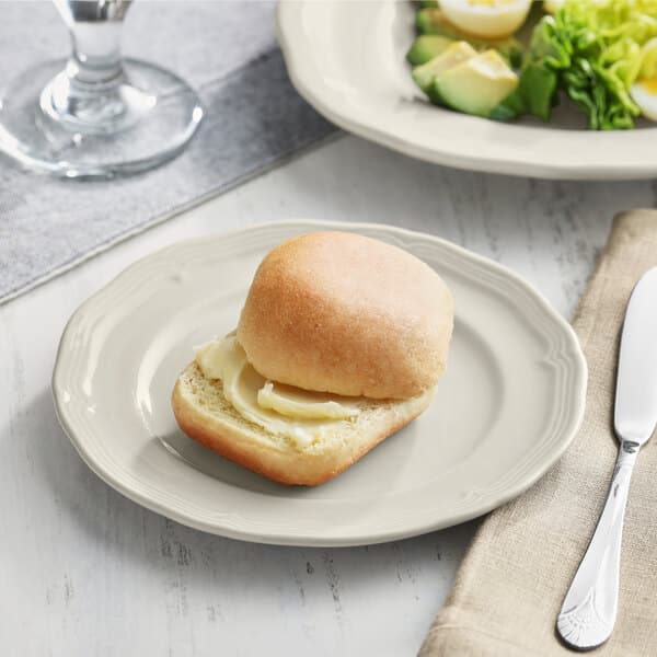 A sample Acopa Condesa scalloped wide rim porcelain plate with a sandwich and salad on it with a buttered roll.