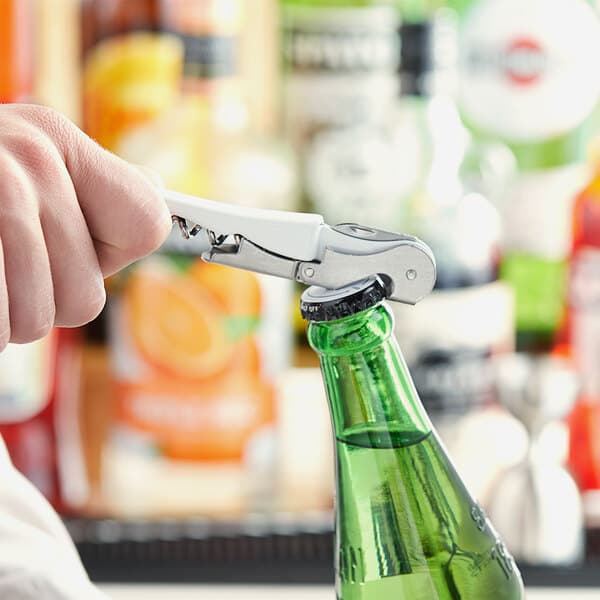 A hand using an Acopa waiter's corkscrew to open a green bottle on a counter.