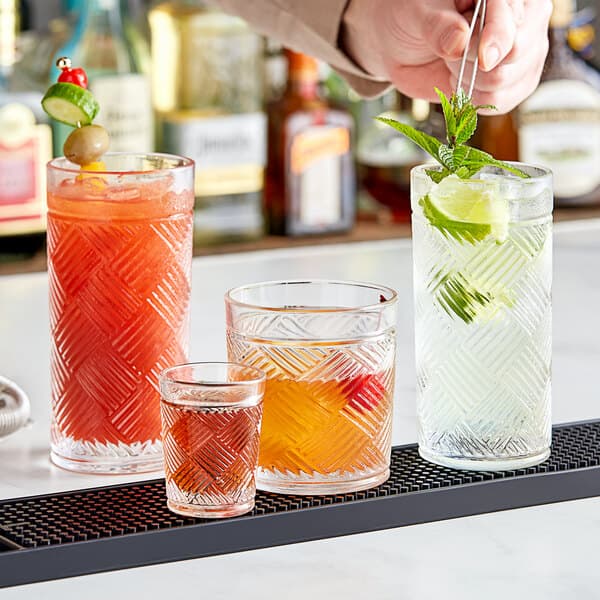 A bartender using tongs to pour different colored drinks into an Acopa Zion beverage glass on a table in a cocktail bar.