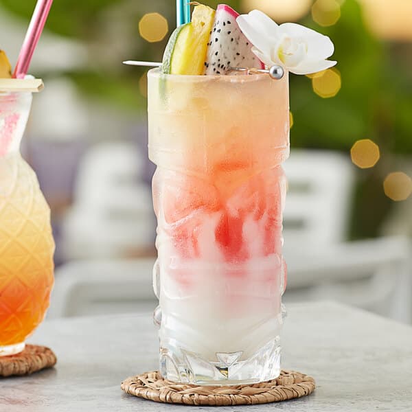 A table set with two Acopa Tiki glasses filled with red and white drinks, ice, and fruit.