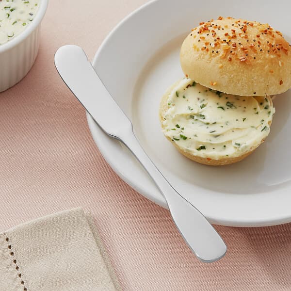 A plate with a roll and a butter knife on it.