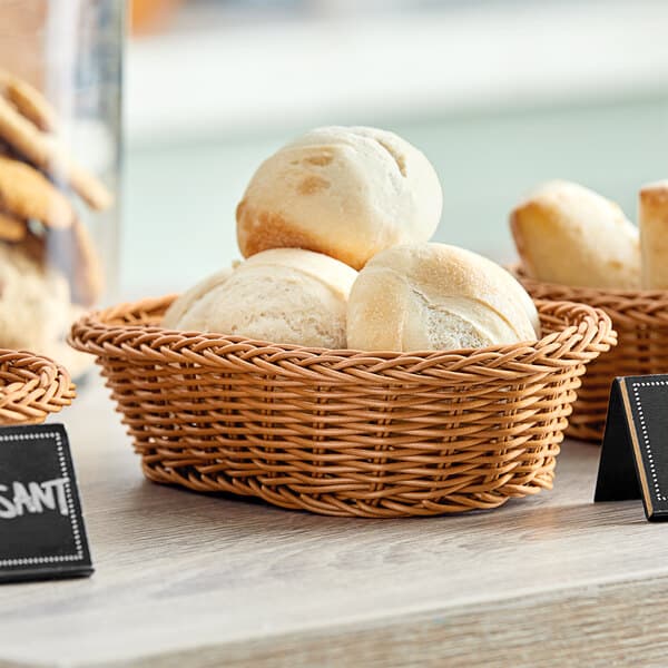 A dark brown Acopa woven plastic rattan bread basket filled with biscuits on a table.