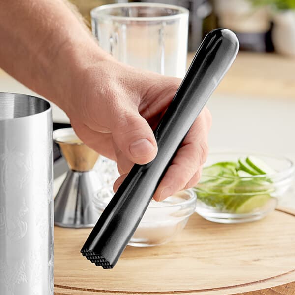 A person holding a black Acopa stainless steel muddler with a tenderizer head.