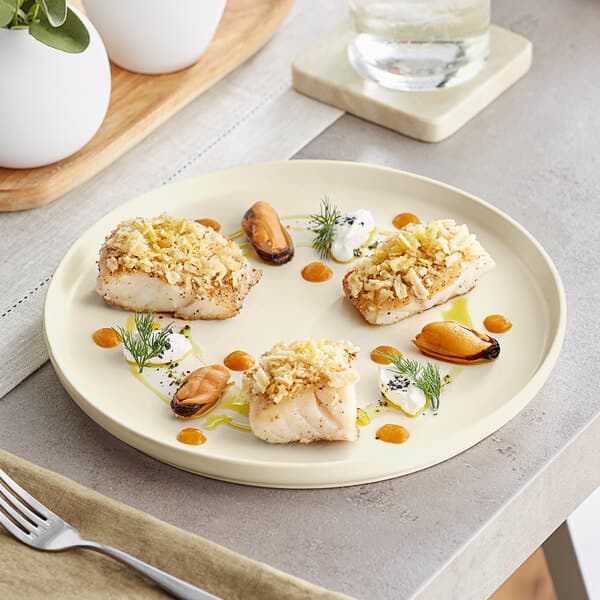 A Acopa Pangea fog white matte coupe porcelain plate with fish and vegetables on it.