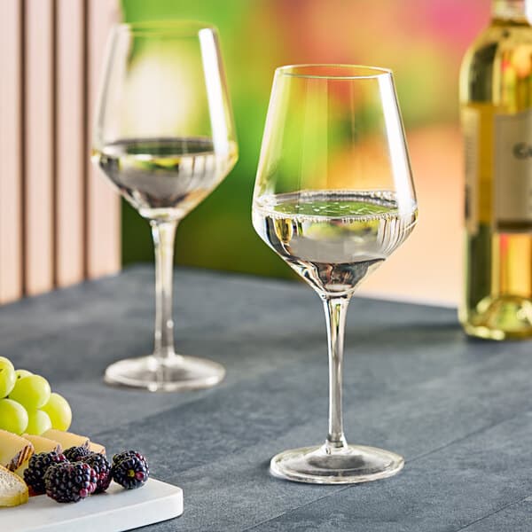 Two Acopa Silhouette wine glasses next to a plate of grapes and a bottle of wine.